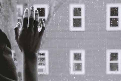 In Graustufen gehaltenes Bild von Hand an einem Fenster während es draußen regnet