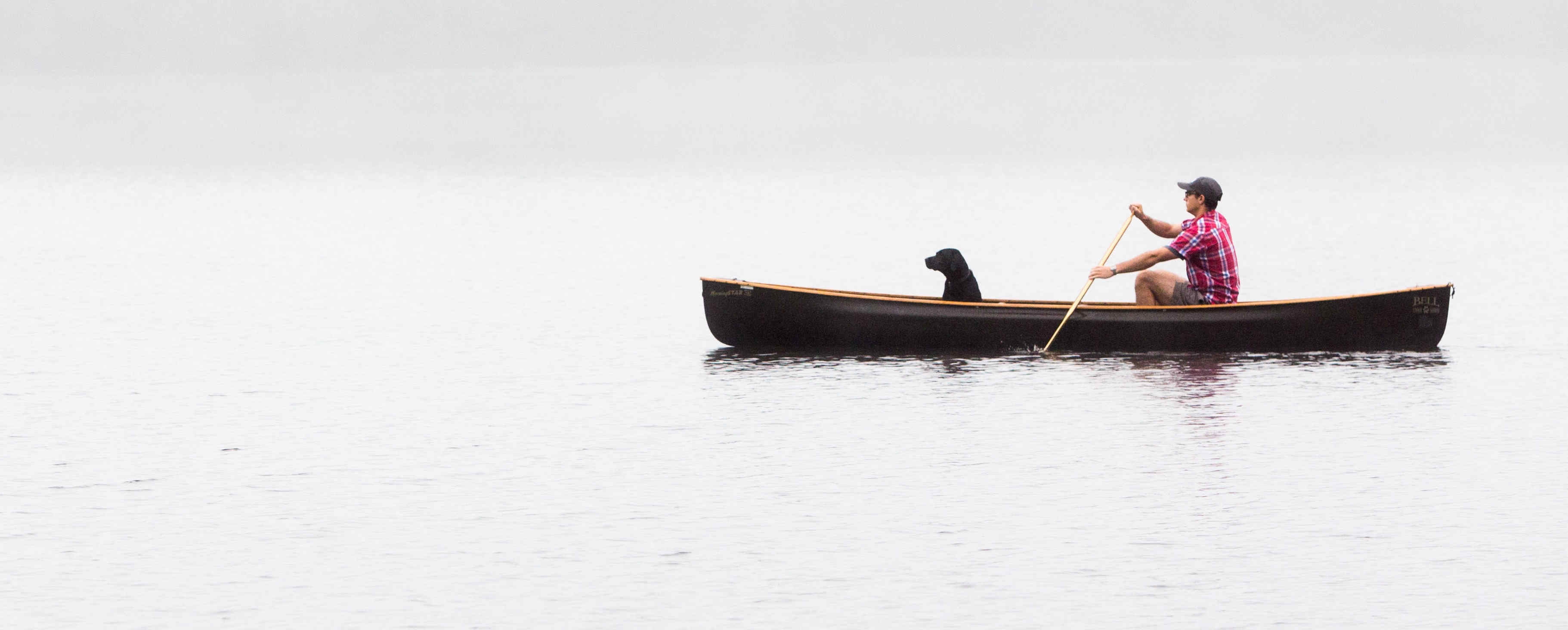 Mann mit Hund sitzen in einem Kanu auf einem See